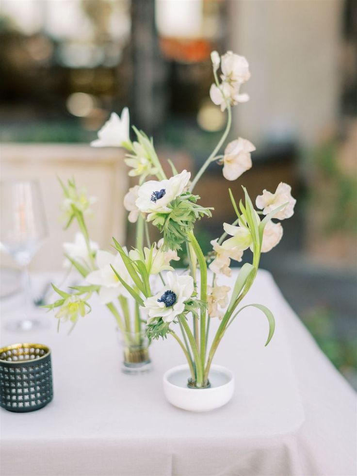 two vases filled with flowers sitting on top of a white table cloth covered table