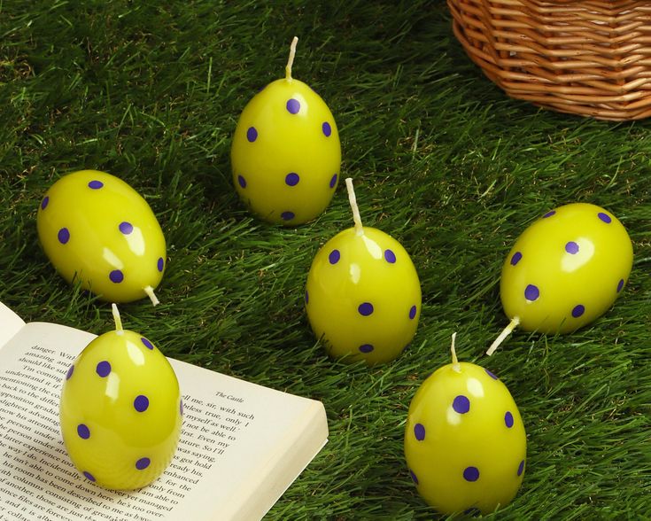 five yellow and blue polka dot candles sitting on the grass next to an open book