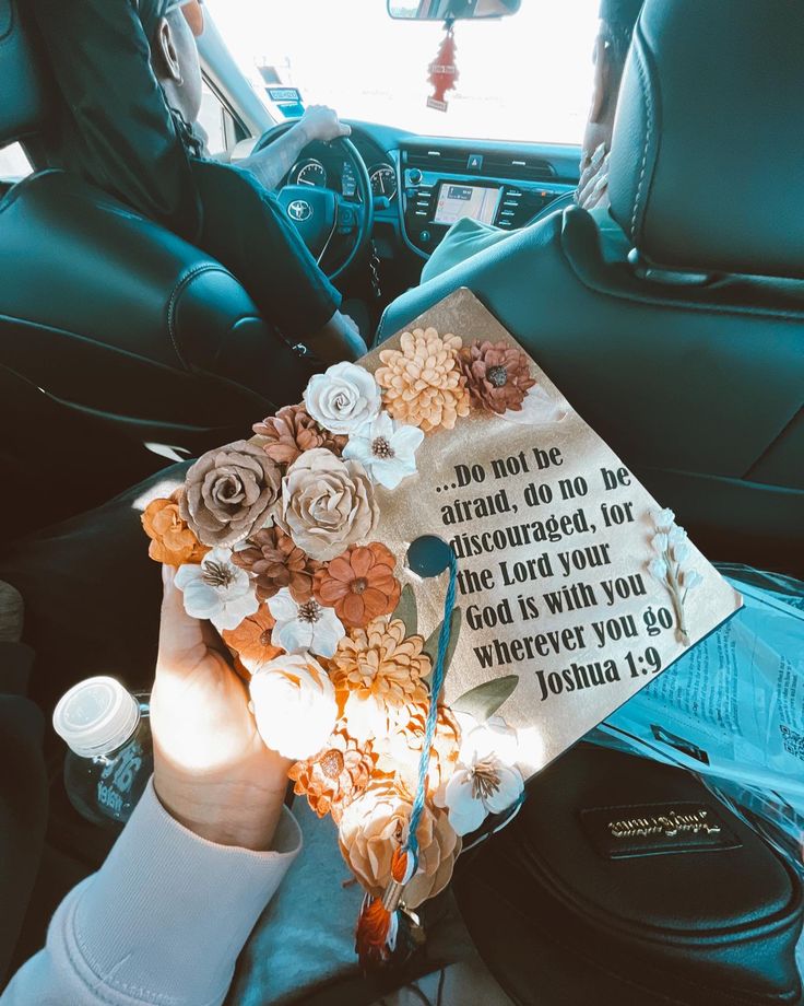 someone holding up a graduation cap with flowers on it in the back seat of a car