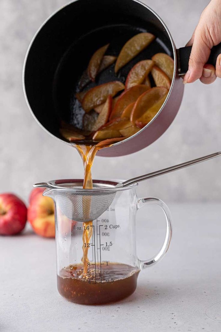 someone pouring caramel sauce on apples in a measuring cup