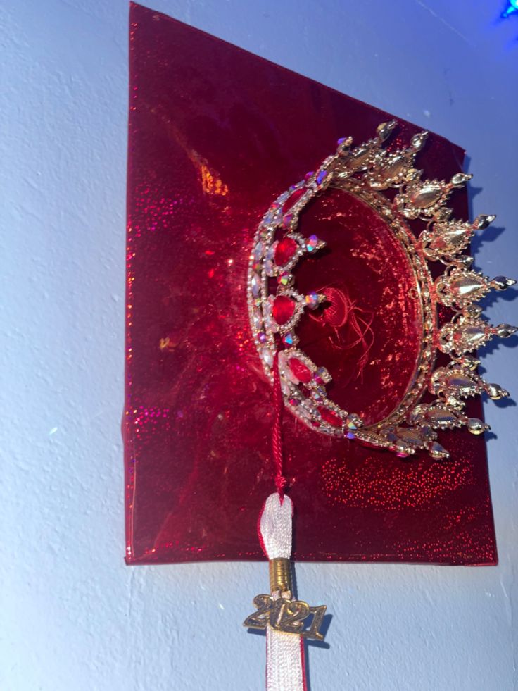 a red wall hanging with a tiara on it's side and a cross in the middle