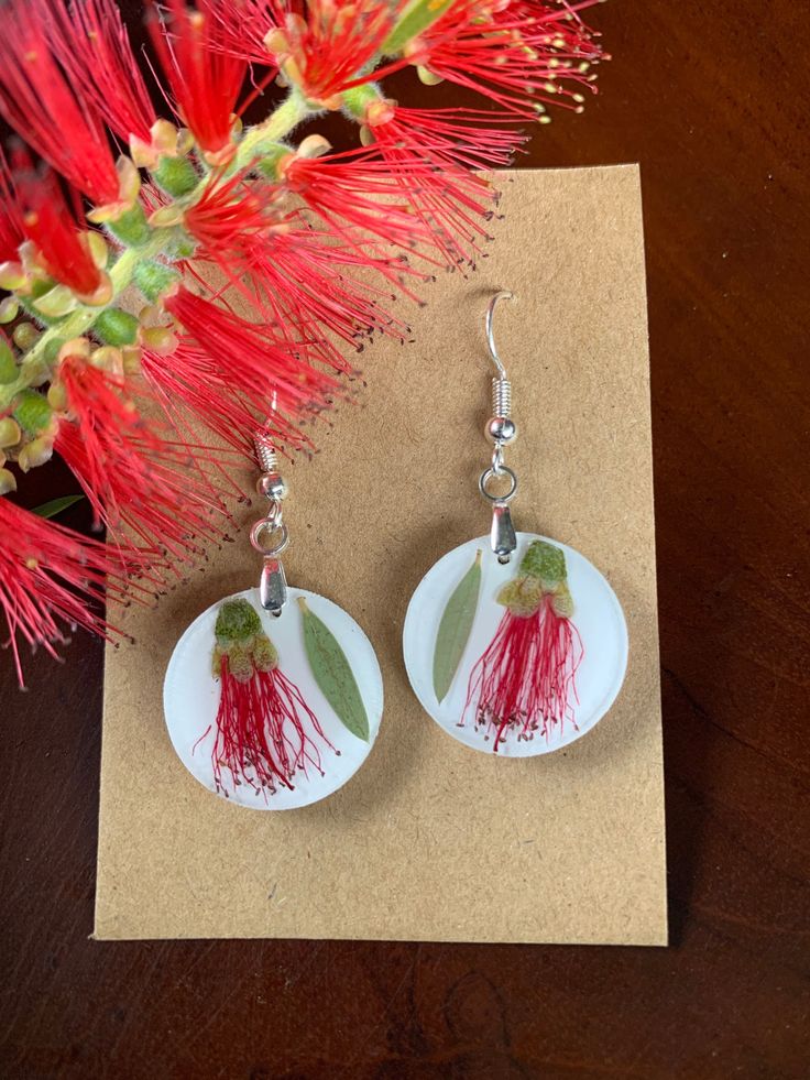 a pair of earrings sitting on top of a piece of paper next to a red flower