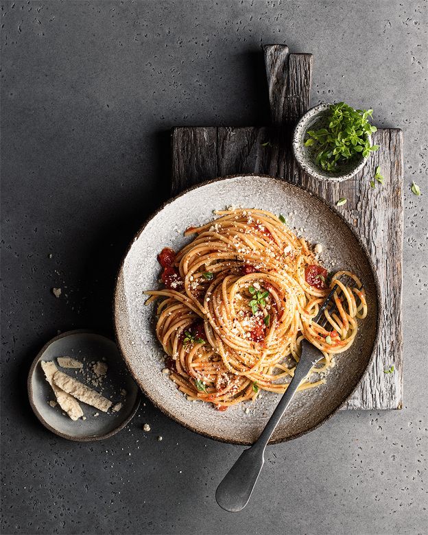 a plate of pasta with sauce, parmesan cheese and herbs on the side