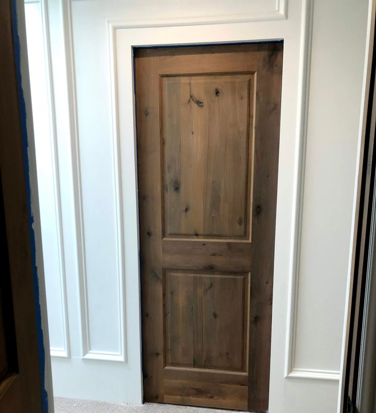 a wooden door in the corner of a room with white walls and carpet on the floor