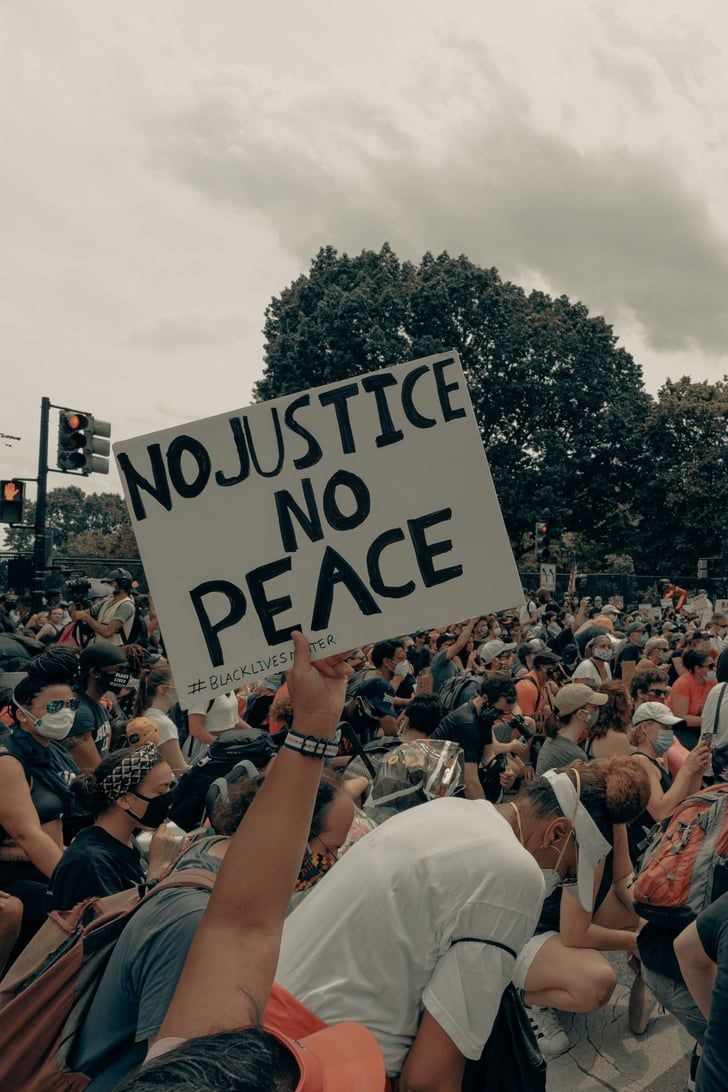 a protester holds up a sign that reads no justice, no peace in front of a large crowd