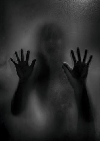 two hands reaching out from behind a glass door with the light shining on them and fog in the air