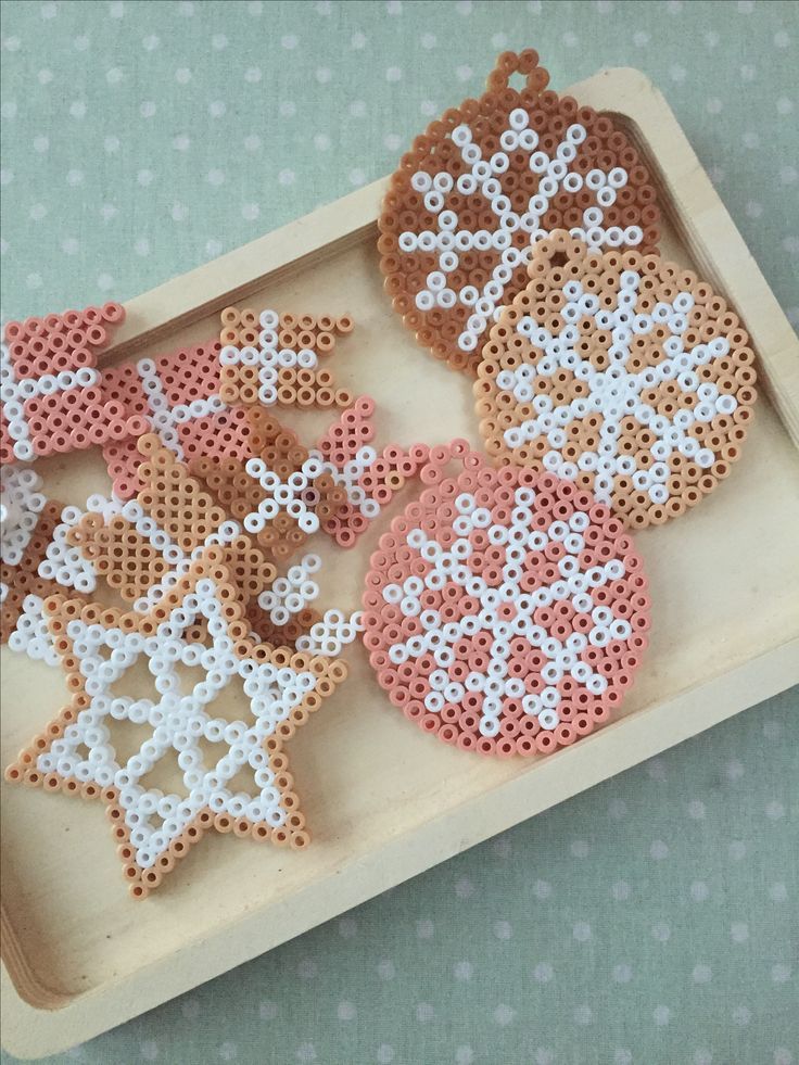 some cross stitch ornaments are sitting on a wooden tray with polka dot dots in the shape of snowflakes