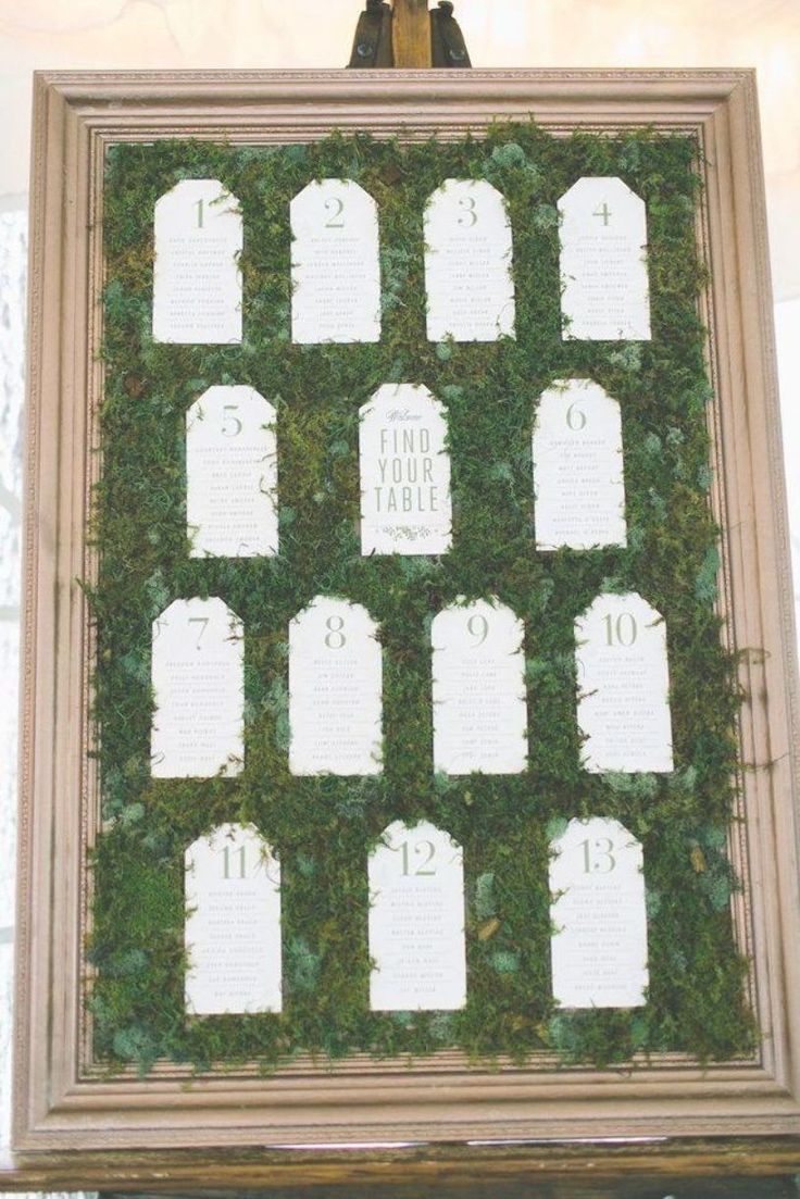 a wedding seating chart is displayed in front of a frame with moss growing on it