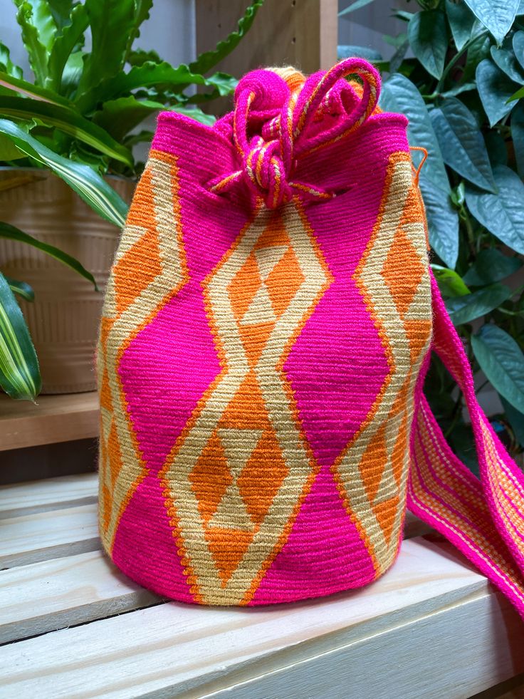 a pink and orange bag sitting on top of a wooden bench next to a potted plant