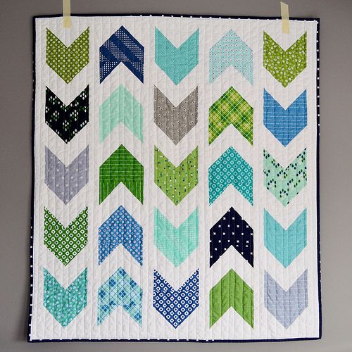 a quilted wall hanging on the side of a gray wall with green, blue and grey chevrons