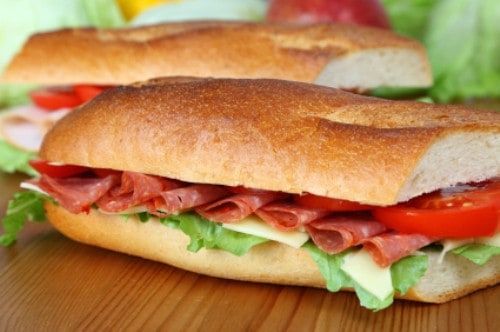 two sub sandwiches with lettuce, tomato and meat on them sitting on a table