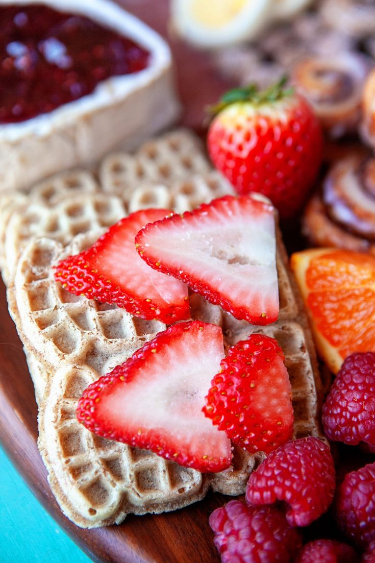 waffles with strawberries, oranges and raspberries on them next to some fruit