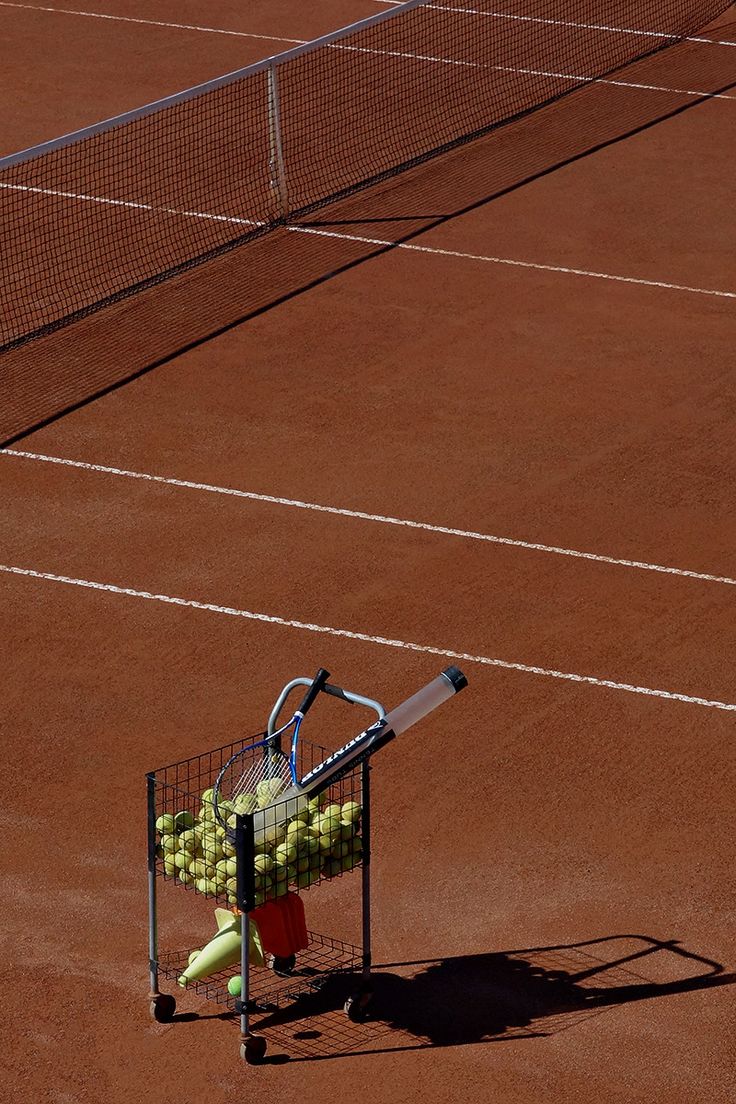 a tennis racket and some balls in a cart on a clay court with white lines