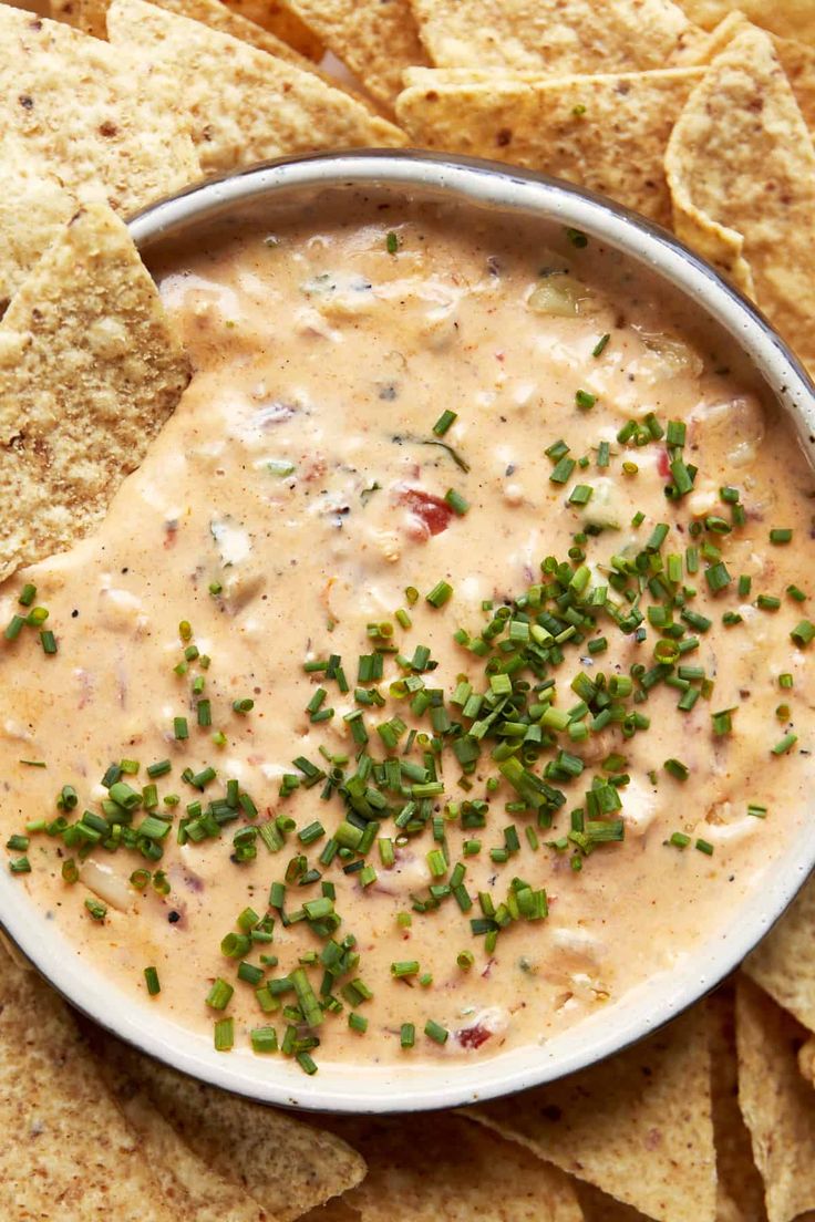 a white bowl filled with dip surrounded by tortilla chips and chopped green onions