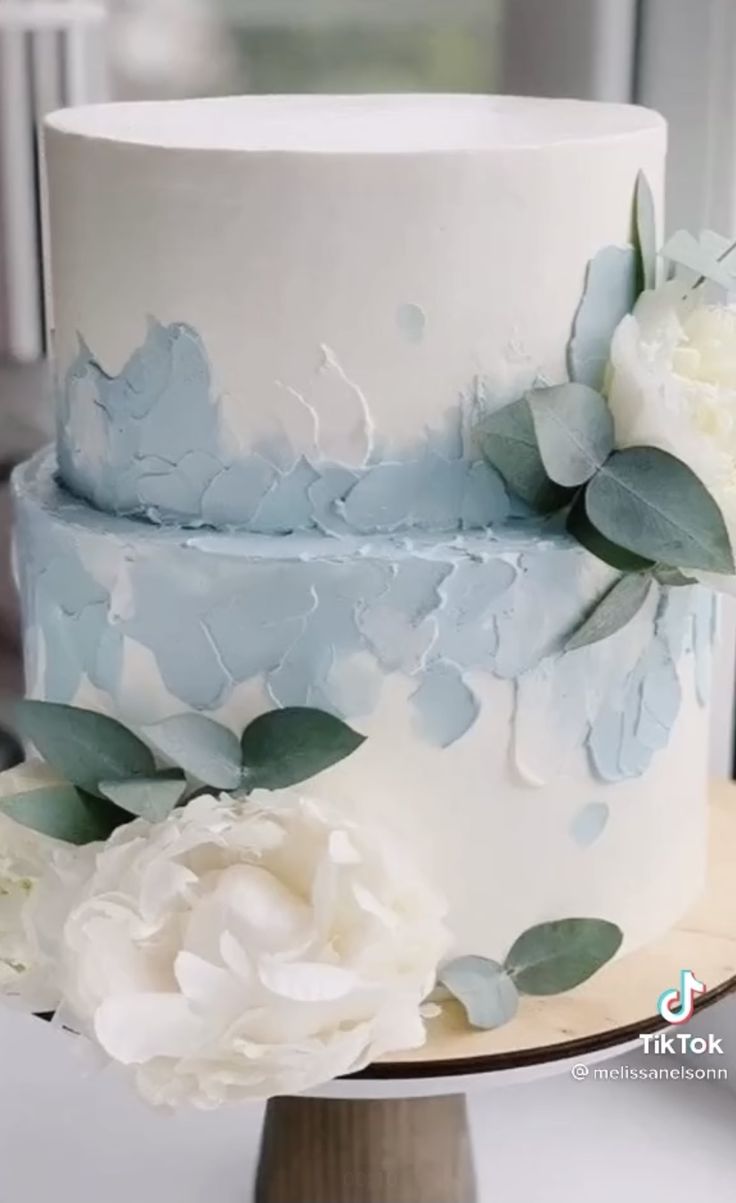 a white and blue wedding cake with flowers on top