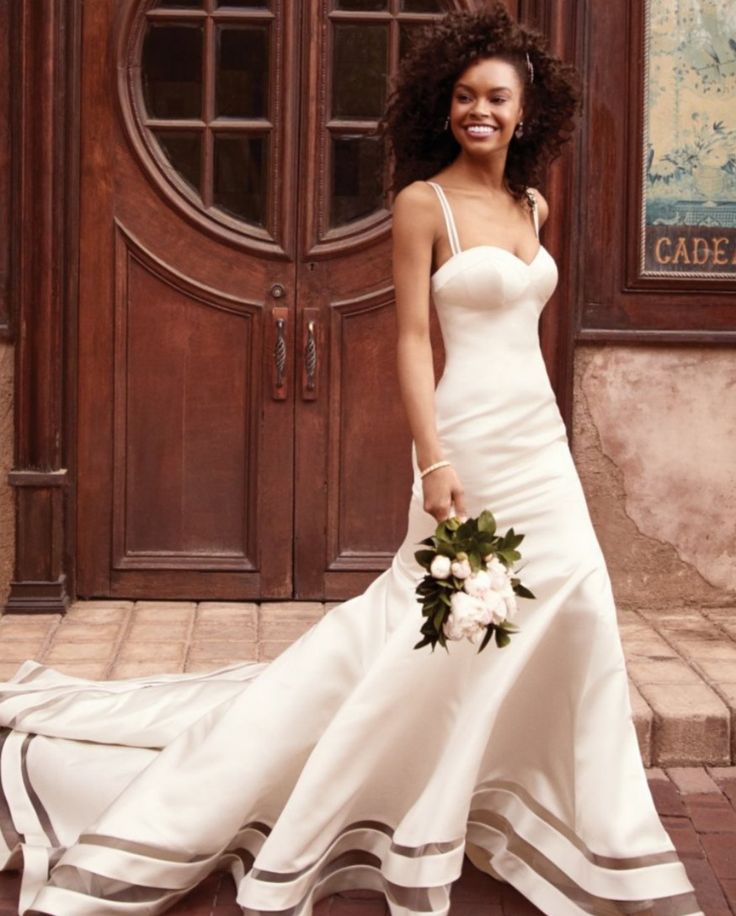 a woman in a white wedding dress standing on a brick floor next to a wooden door