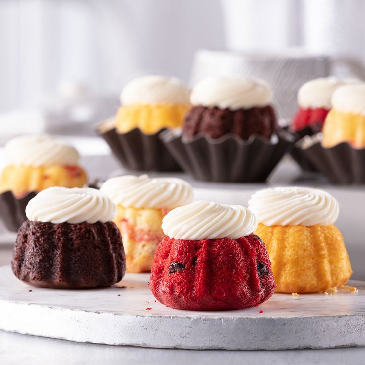 several cupcakes with white frosting and red velvet on a marble platter