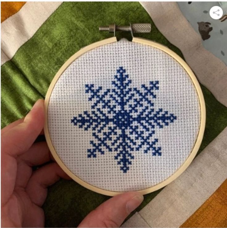 a hand holding a cross stitched snowflake