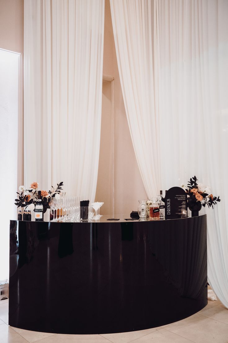 a black curved counter with flowers on it in front of a white curtained window