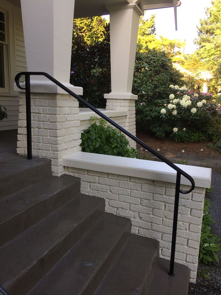 there is a white brick wall and black metal handrails on the front steps