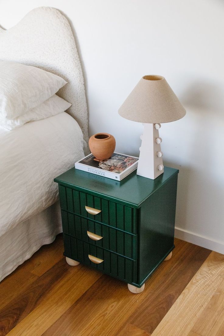 a green nightstand next to a bed with a lamp on it and a book sitting on top