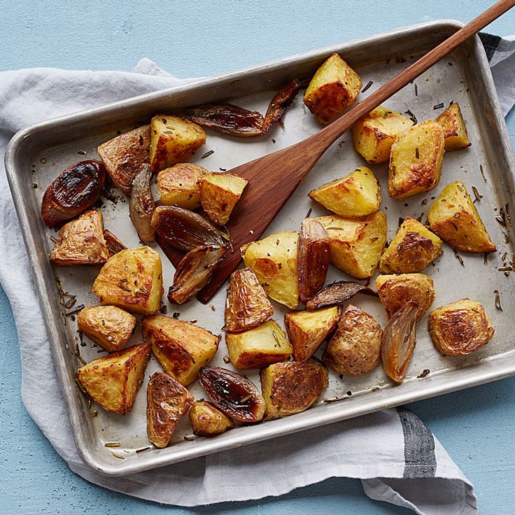 a pan filled with cooked potatoes on top of a blue table cloth next to a wooden spoon