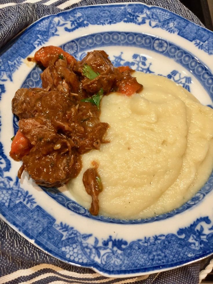 a blue and white plate topped with mashed potatoes and beef stew next to gravy