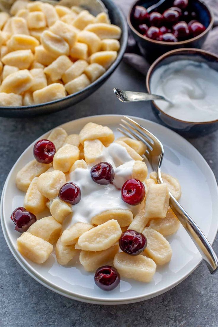 a plate with fruit and yogurt on it next to bowls of cherries