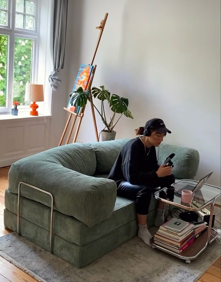 a woman sitting on top of a green couch in a living room next to a window