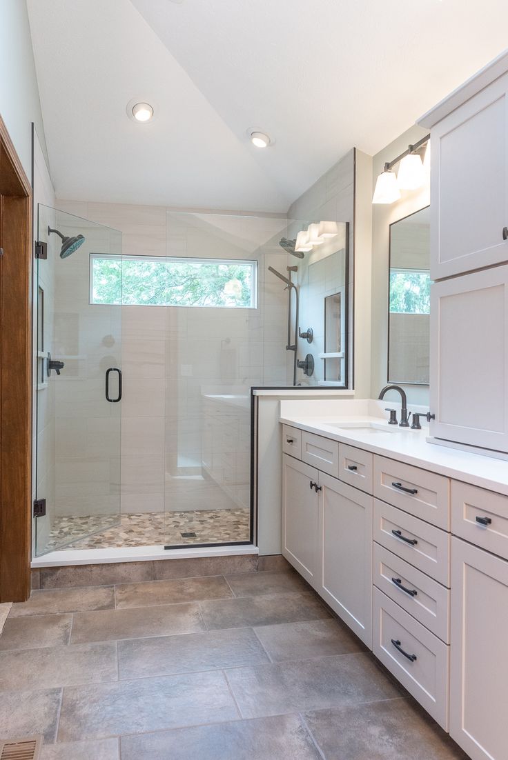 a bathroom with two sinks and a walk in shower next to a large white cabinet