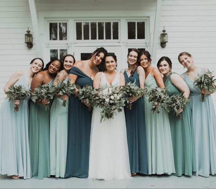 a group of women standing next to each other in front of a white building holding bouquets