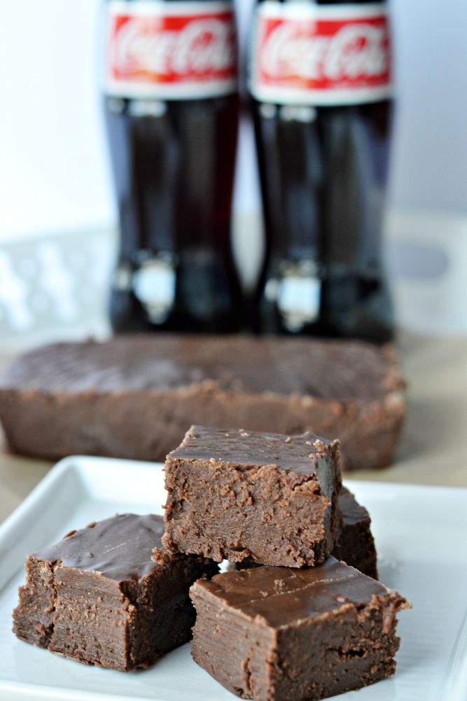 three pieces of chocolate fudge brownies on a white plate with coca - cola bottles in the background