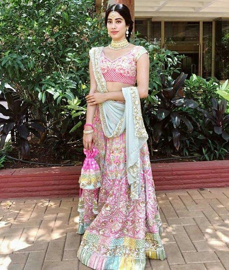 a woman in a pink and blue lehenga standing on a brick walkway with her arms crossed