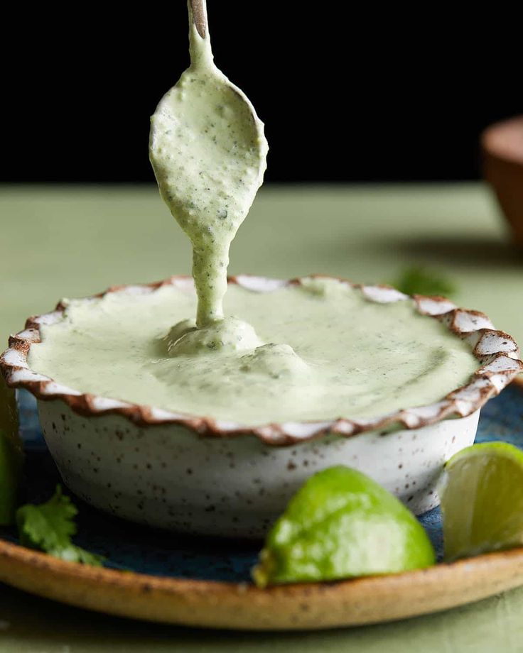 a spoon dipping some type of sauce into a bowl with limes on the side