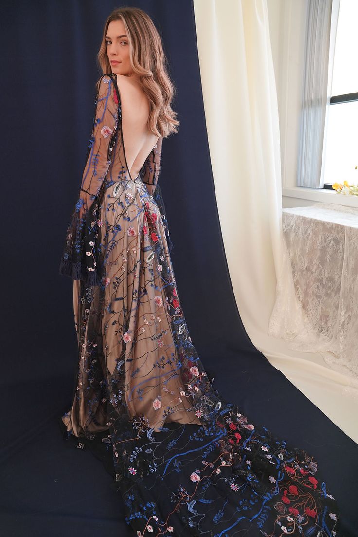 a woman standing in front of a window wearing a long dress with flowers on it