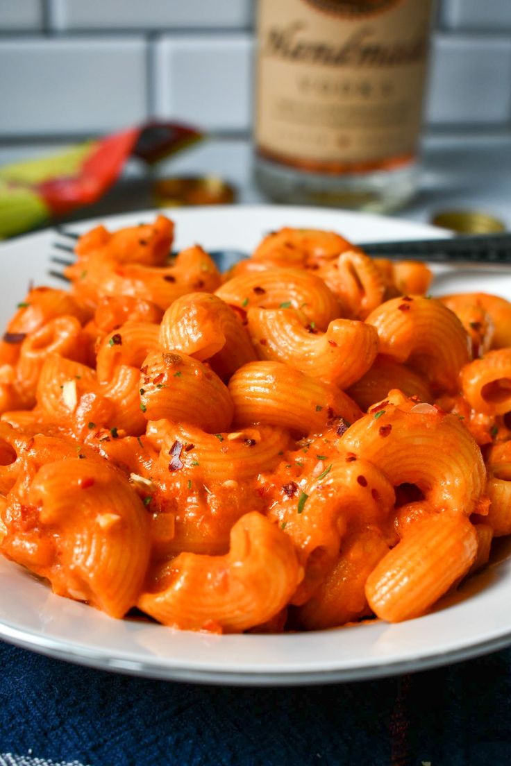 a plate full of macaroni and cheese with a bottle of wine in the background