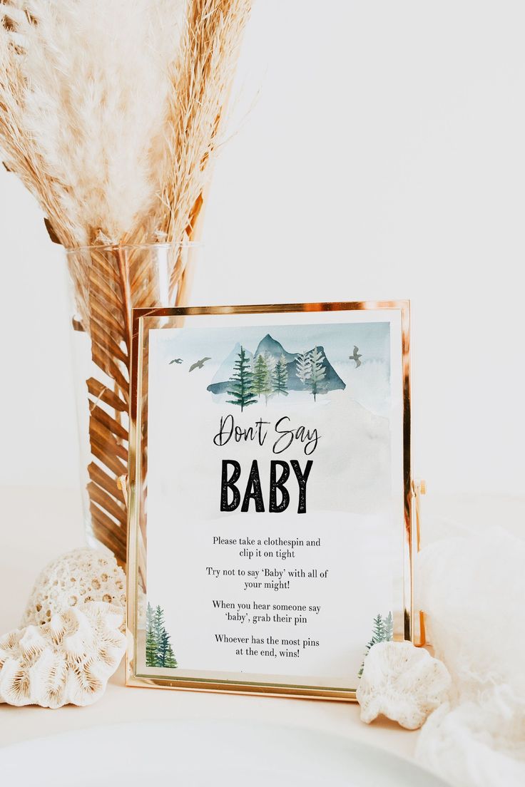 a baby shower sign sitting on top of a table next to a vase filled with feathers