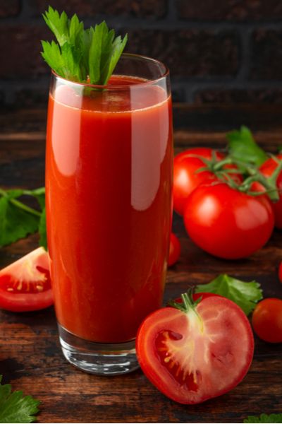 a glass filled with tomato juice next to tomatoes and parsley on a wooden table