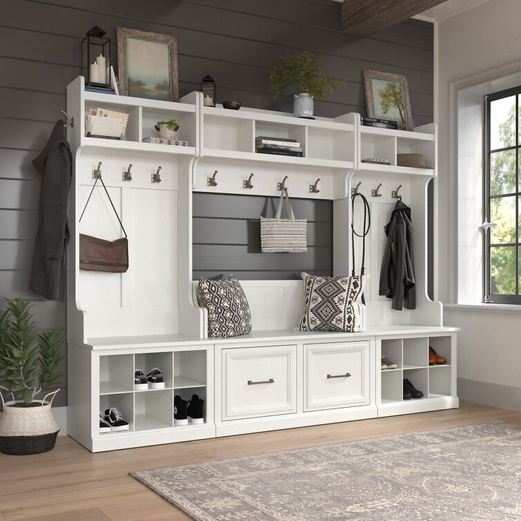 a room with some white shelves filled with coats and shoes next to a rug on the floor