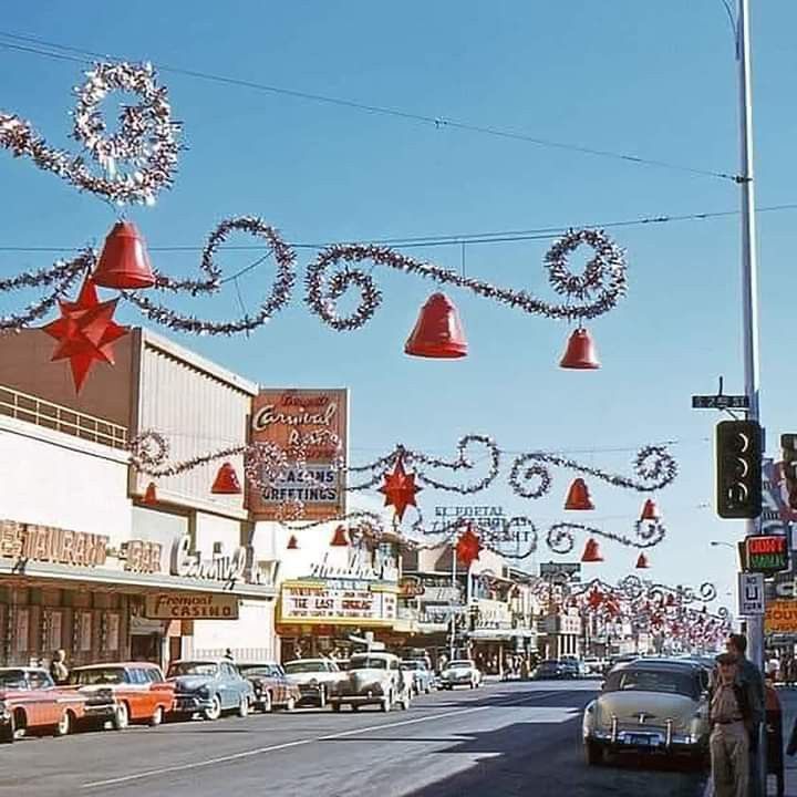 a street with cars parked on the side of it and christmas decorations hanging from the buildings