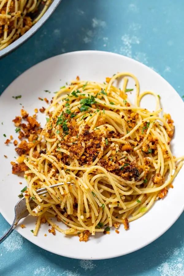 a white plate topped with spaghetti next to a bowl of meat and sauce on a blue table