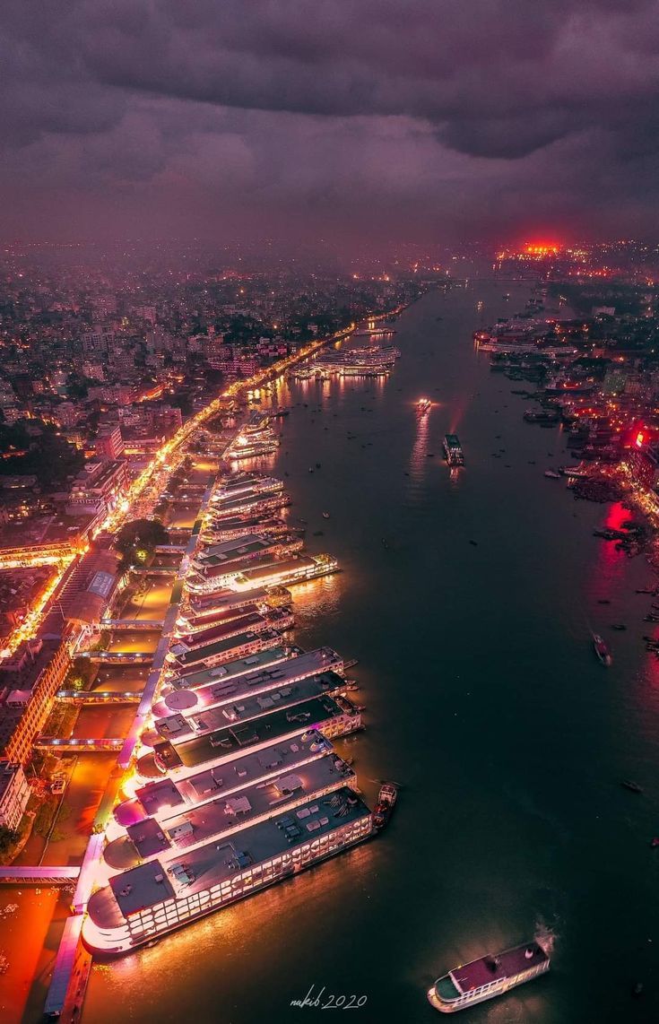 an aerial view of boats docked in the water at night, with lights on them