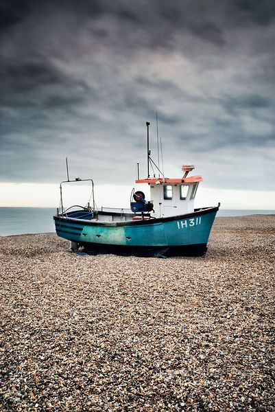 a blue boat sitting on top of a beach next to the ocean under a cloudy sky