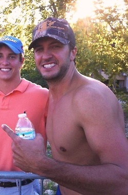 two shirtless men posing for the camera with drinks in their hands and trees in the background