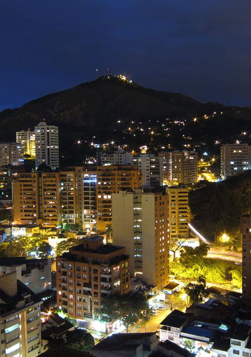 the city is lit up at night with mountains in the backgrouds and buildings on both sides