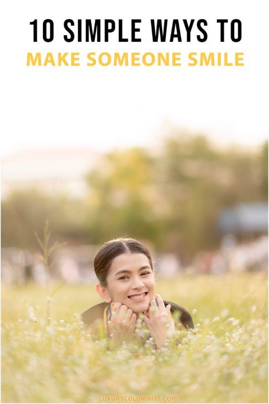 a woman laying in the grass with her hands under her chin and smiling at the camera