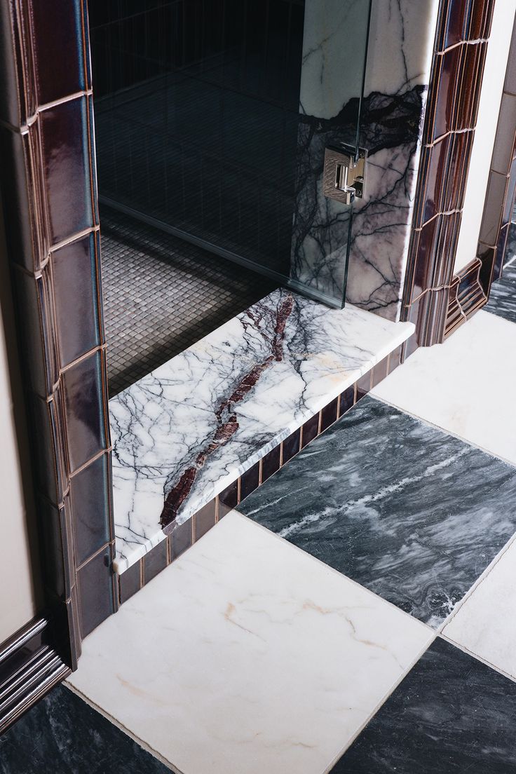 Primary bathroom and master bathroom design with dark and moody aesthetic. Burgundy tile wall in gloss finish, marble checkerboard tile on floor. Light oak wood vanity with marble vanity top. Brass sconces on either side of vanity mirror. Jean Stoffer Design, Jean Stoffer, Ann Sacks Tiles, Trend Tiktok, Ann Sacks, Red Tiles, Primary Bathroom, Glazed Ceramic Tile, Deep Maroon