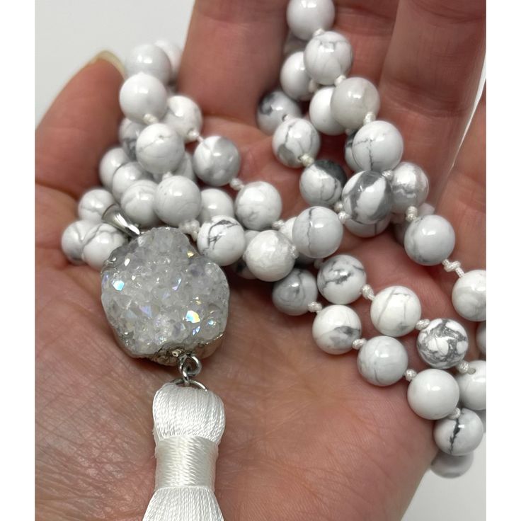 This carefully hand crafted Howlite Mala with Stone features a combination of white howlite gemstones and a white silk tassel for a beautiful, calming aesthetic. The mala is tied together with strong silk thread, designed to last and retain its original beauty.Howlite is a stone known to bring calm to the wearer, it's often worn as a reminder of patience. The marbled stone is associated with inner calm, stress release, and calming an over active mind. The necklace is made of:- High quality, 108 Adjustable White Tassel Necklace, Elegant White Hand-wrapped Necklace, Elegant White Hand Wrapped Necklace, Adjustable White Necklace With Gemstone Beads, Adjustable White Gemstone Bead Necklaces, White Hand Knotted Jewelry With Round Beads, White Hand Knotted Bohemian Necklace, White Bohemian Hand Knotted Necklace, White Bohemian Hand-knotted Necklace