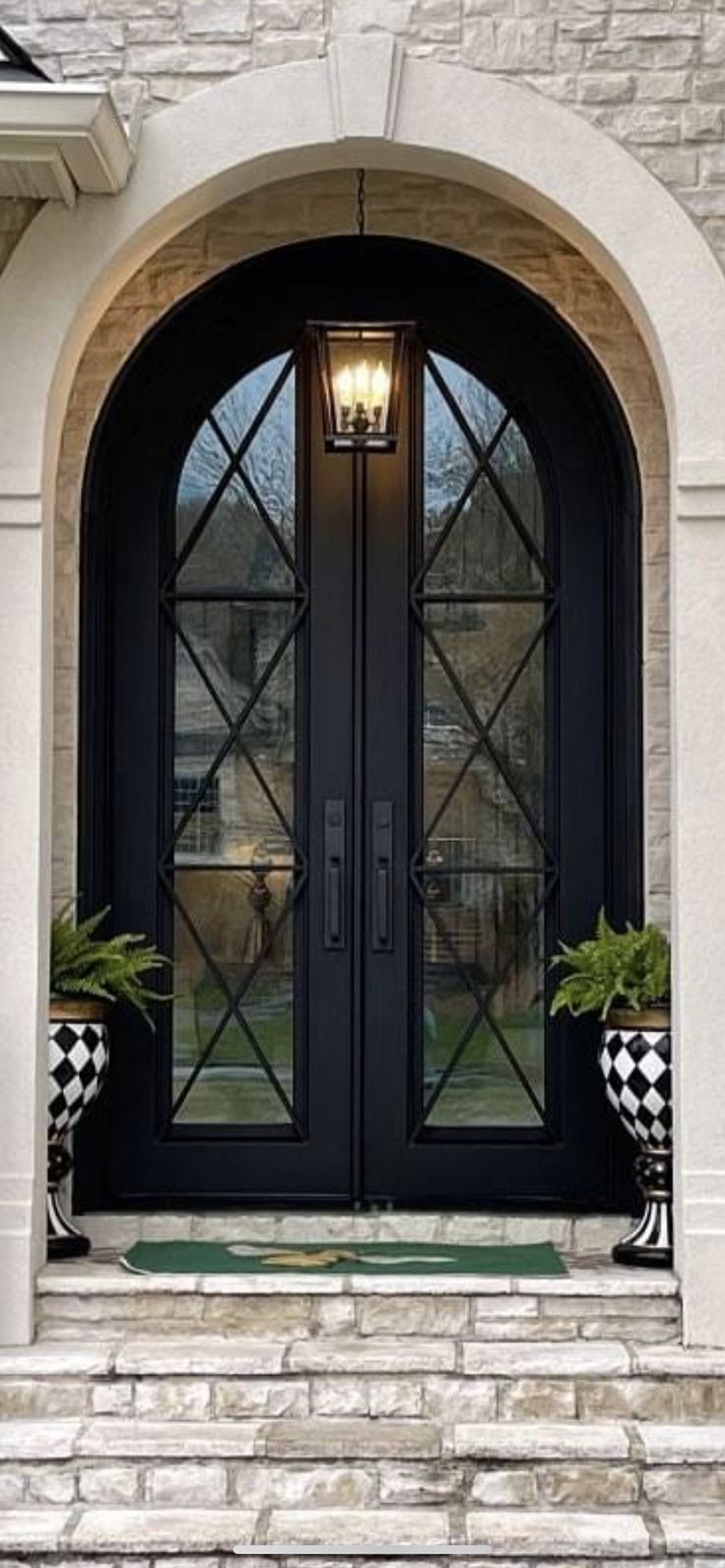 a black double door with two checkered planters on each side and an arched glass front door