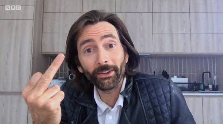 a man with long hair and beard making a face while pointing to the side in front of him